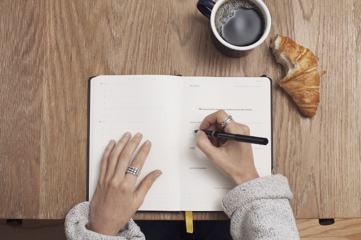 A woman writing her goals in a journal over coffee